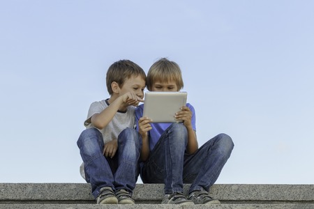 Two boys sitting and looking at tablet pc. Childhood, education, learning, technology, leisure conceptの写真素材