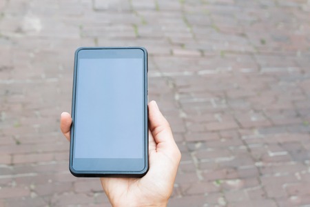 Modern black mobile phone in a woman's hand. Urban backgroundの写真素材