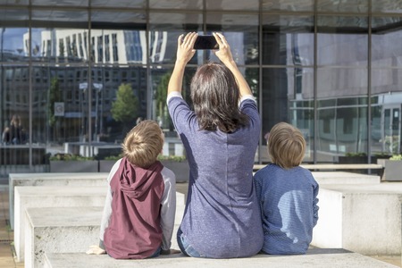 Mother and children taking selfie portrait on smartphone outdoors. Back view. Family, childhood, technology and people conceptの写真素材