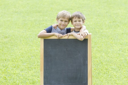 Two little boys standing at the blackboard outside. Green background. Copy space for text.の写真素材