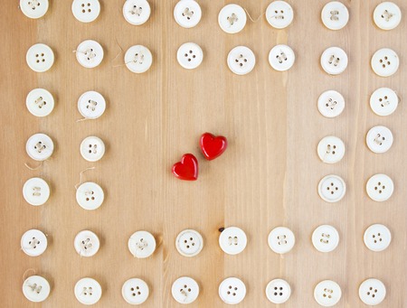 Old vintage buttons frame border with two red wooden hearts in the middle on wooden background. Sewing, hobby, lifestyle conceptの写真素材