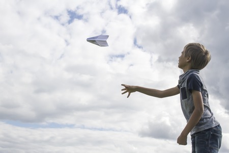 Boy flying a paper plane against blue sky. Low angle viewの写真素材