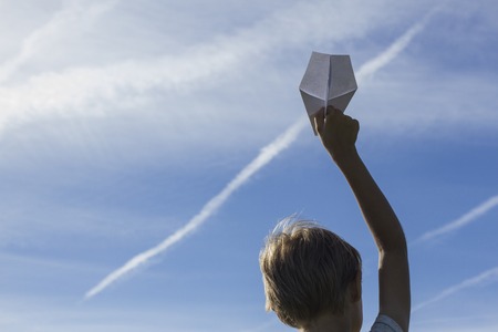 Little boy with paper plane in his hand against blue sky. Low angle viewの写真素材
