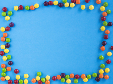 Frame of multicolored small candie on blue background. Copy space for text. Flat lay.の写真素材