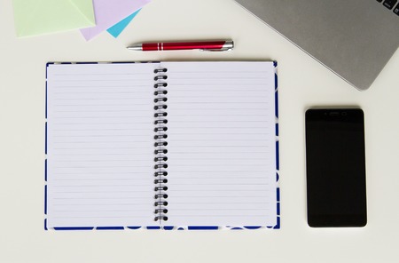 White desk with laptop keyboard, open colourful notebook, envelops, red pen and mobile phone. Flat lay, top viewの写真素材