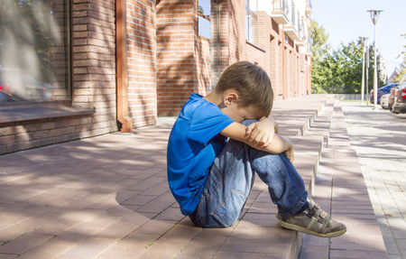 Sad, lonely, unhappy, disappointed, alone child sitting alone on the ground. City background Outdoorの写真素材