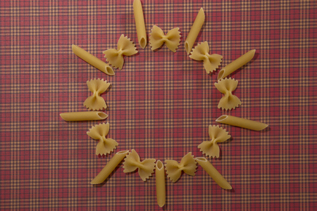 Dry wholemeal penne and bow tie pasta on red squared background. Flat lay. Top view. Copy spaceの写真素材