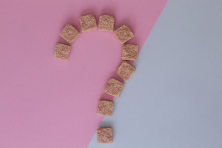 Brown sugar cubes shaped as a question mark on colourful background. Top view. Diet unhealty sweet addiction conceptの写真素材