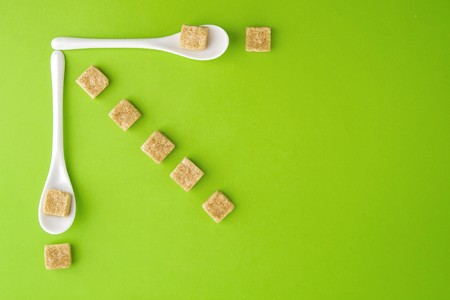Brown sugar cubes and white spoons on greenery background arringed in rows. Top view. Flat lay. Copy space for text. Diet unhealty sweet addiction conceptの写真素材