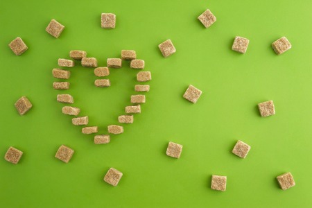 Sugar cubes shaped as heart on greenery background. Top view. Diet unhealty sweet addiction conceptの写真素材