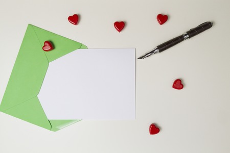 Green envelope, message, pen and small red hearts on white table. Love letter, valentines day conceptの写真素材