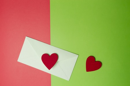 Envelop with two hearts on greenery and red colored paper background. Top view. Copy space for textの写真素材