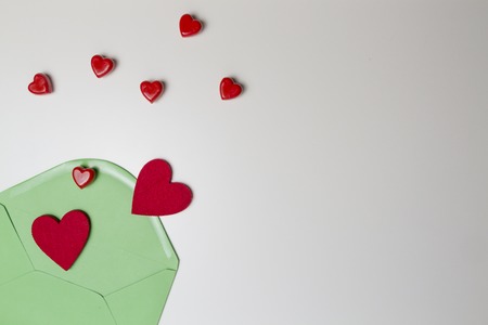 Green envelope and red hearts on white table. Top view.の写真素材