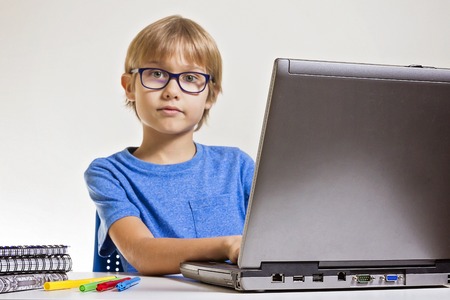 Boy with glasses using laptop computer while sitting on desk at home. Technology, education concept