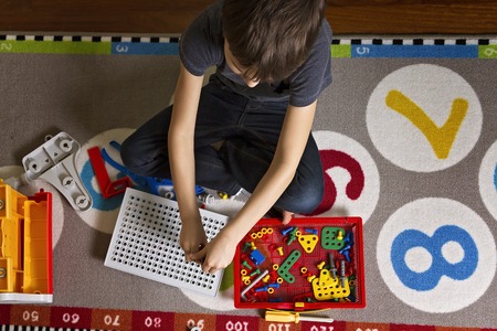 Child playing with toys tool kit while sitting on the floor in his room.Top view