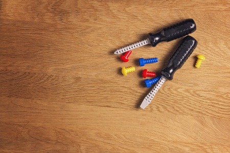 Kids construction toys tools: colorful screwdrivers, screws and nuts on wooden background. Top view. Flat lay. Copy space for textの写真素材