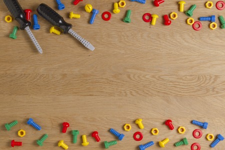 Kids construction toys tools: colorful screwdrivers, screws and nuts on wooden background. Top view. Flat lay. Copy space for textの写真素材