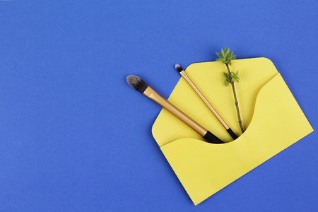 Make up brushes with spring gentle leaves and buds on small tree twigs in yellow envelope on blue backgroundの写真素材