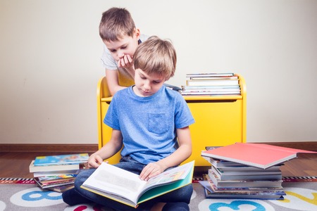 Kids reading a book. Boy reads a story to his brother at homeの写真素材