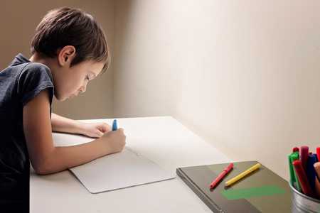 Boy sitting at the desk home and doing his homework. Child writting. School, children, education conceptの写真素材