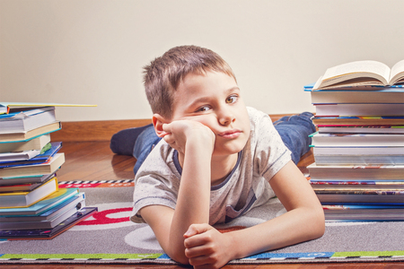 Bored child lying between piles of booksの写真素材