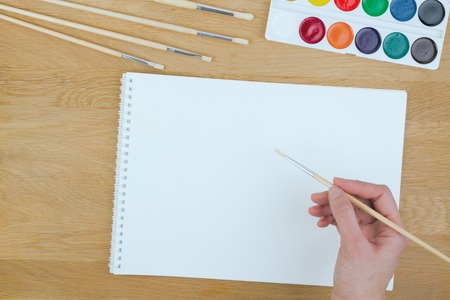 Top view of a hand with painting brush, watercolor paints and blank sheet of paperの写真素材
