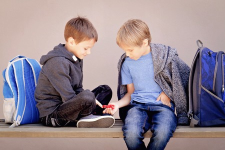 Primary education, school, friendship concept - two boys with backpacks sitting, talking and playing with spinnerの写真素材