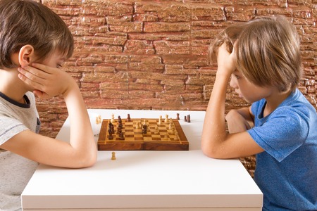 Two children playing chess at the tableの写真素材