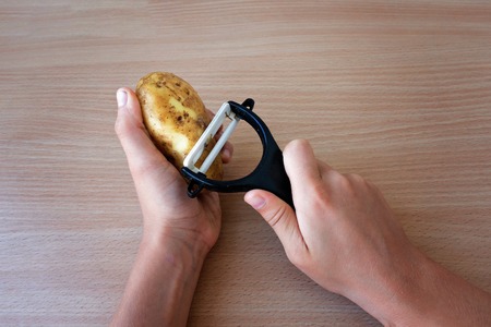 Hands peeling potato with black peelerの写真素材