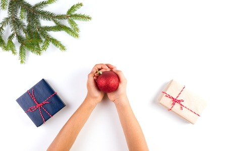 Top view of kid hands holding christmas decoration. Gift boxes and christmas tree branch on white tableの写真素材