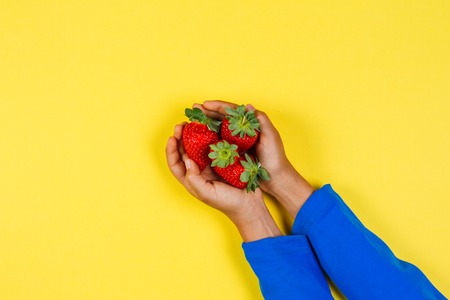 Kid hands holding fresh strawberries on yellow background