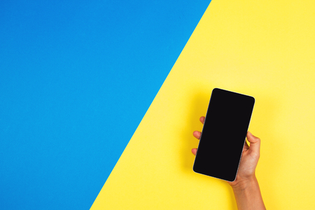 Hand holding the phone on blue and yellow backgroundの写真素材
