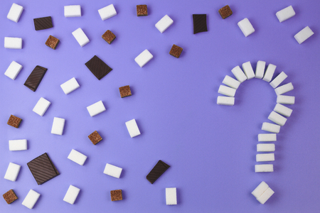 Sugar background. Sugar cubes shaped as a question mark sign, brown and white sugar cubes and chocolate pieces on purple background.の写真素材