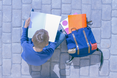 Child sitting on the ground and flipping through notebook pagesの写真素材