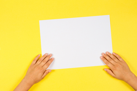 Kids hands with white blank paper card on yellow backgroundの写真素材