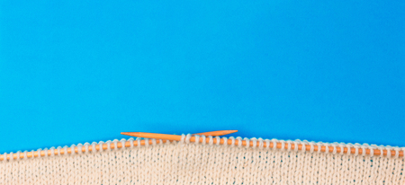 Top view of knitting with two bamboo knitting needles on blue backgroundの写真素材
