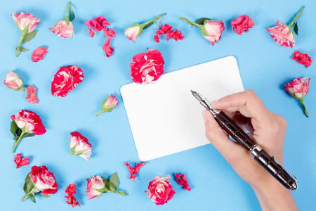 Woman hand writing on blank card.Fresh roses on blue backgroundの写真素材