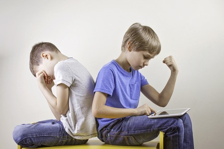 Kids playing computer games with tablet computer. One boy win the game and other sitting tired and unhappy after loosing game.の写真素材