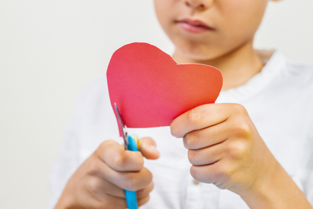 Child hands cutting red paper heart with scissorsの写真素材