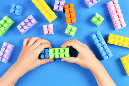 Kids hand playing with colorful plastic construction blocks on blue backgroundの写真素材