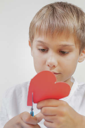 Child cutting red paper heart with scissorsの写真素材