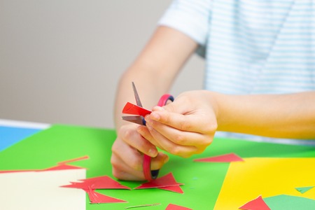 Child hands cutting colored paper with scissors at the tableの写真素材