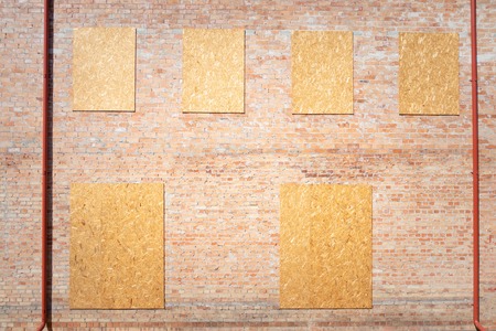Unfinished red brick house facade with chipboard wood covered windows.の写真素材