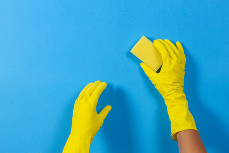 Hands in yellow gloves with sponge on blue backgroundの写真素材