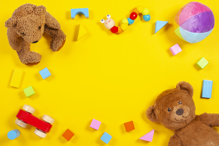 Baby kids toys frame with teddy bear, wooden toy car, colorful bricks on yellow background. Top viewの写真素材