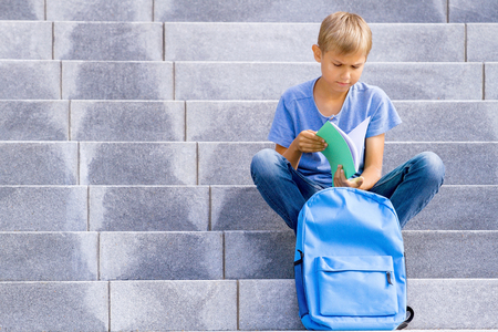 Boy reading book sitting on the stairs outdoorsの写真素材