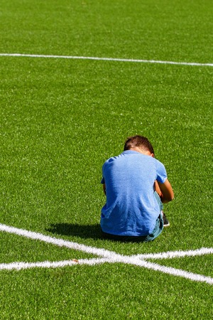 Sad disappointed boy sitting on the grass in stadiumの写真素材