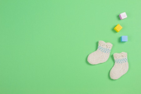 Knitted baby wool socks and wooden bricks on green backgroundの写真素材