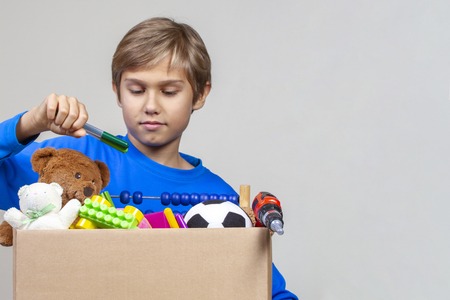 Donation concept. Kid collecting school supplies into donation box with clothes, toys and booksの写真素材