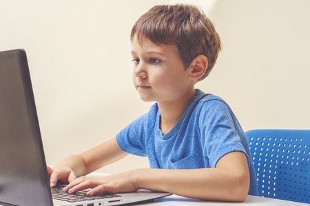 Concentrated boy sitting at desk with laptop computer and doing homeworkの写真素材